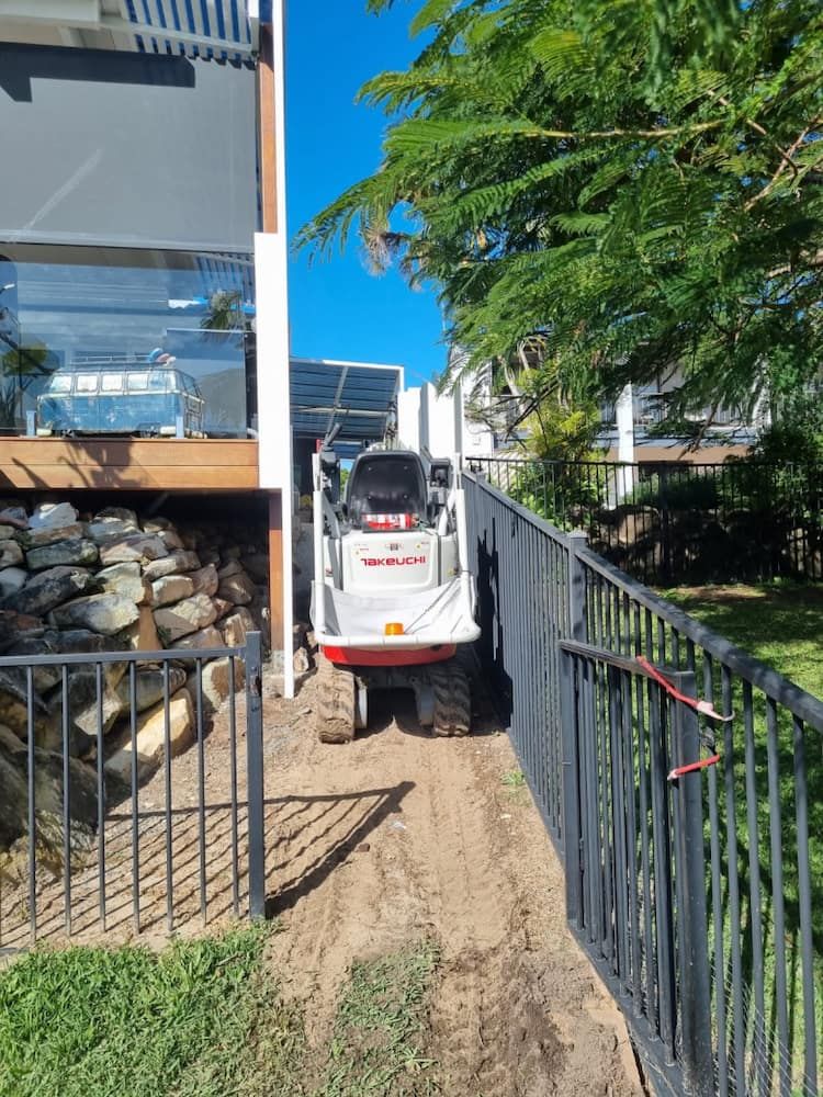 A Small White Bobcat Machine is Driving on a Dirt Path Next to a Black Fence — Coastline Earthworks in Helensvale, QLD