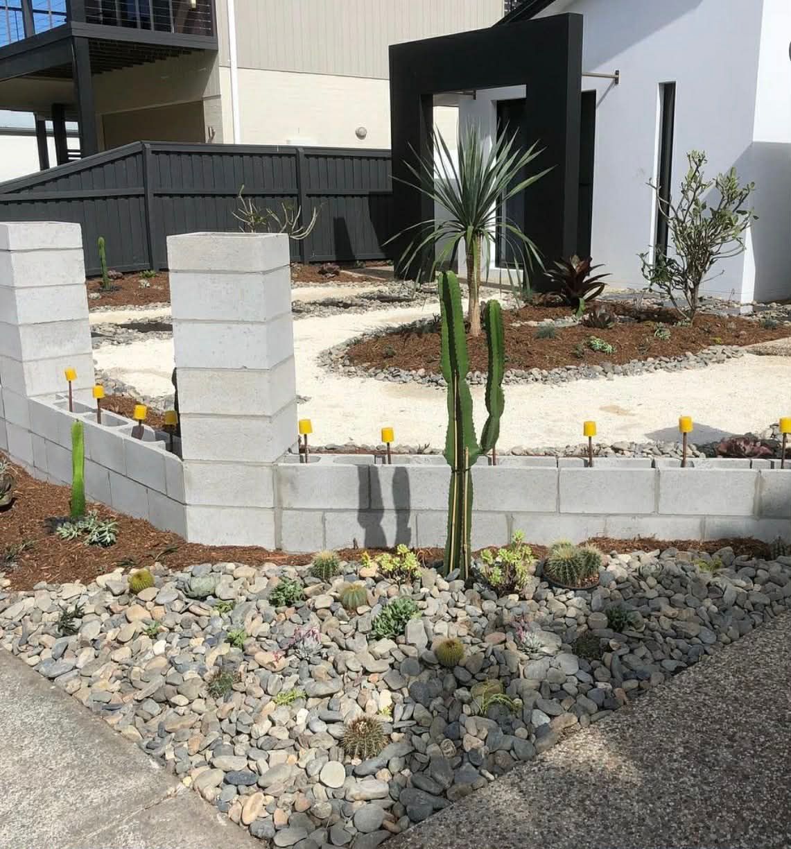 Front yard landscaping with a small cactus, white retaining wall, and gravel bed beside a modern house — Coastline Earthworks in Helensvale, QLD