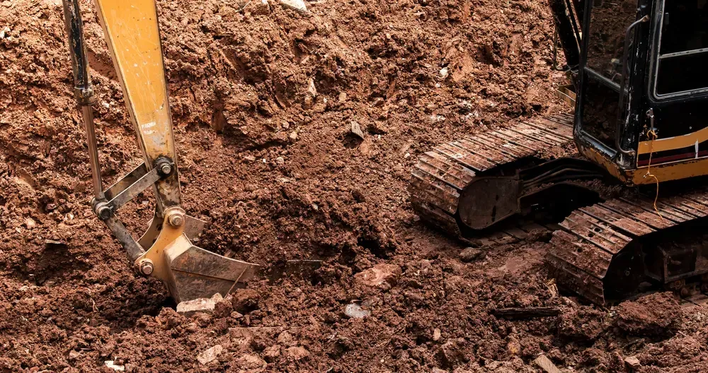 Excavator digging into brown soil, tracks visible. — Coastline Earthworks in Logan, QLD
