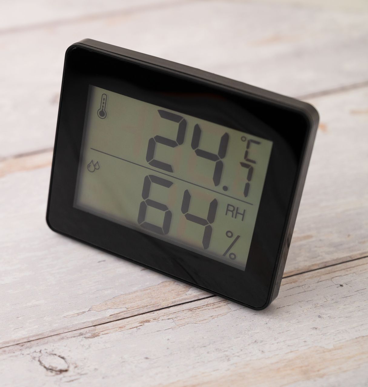 Black digital thermometer displaying 24.7 degrees Celsius and 64% relative humidity.