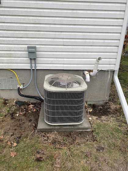 AC unit outside a house, with electrical connections and drainpipe.