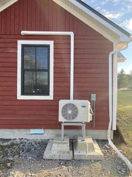 Red building with a window, air conditioner mounted on concrete blocks, and white pipes.