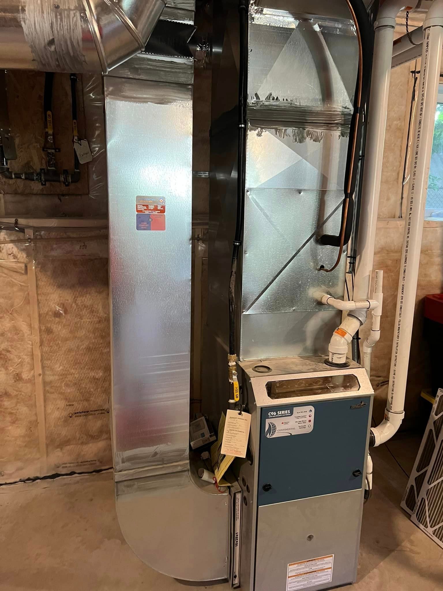 Furnace with ductwork and a white PVC pipe in a basement setting.