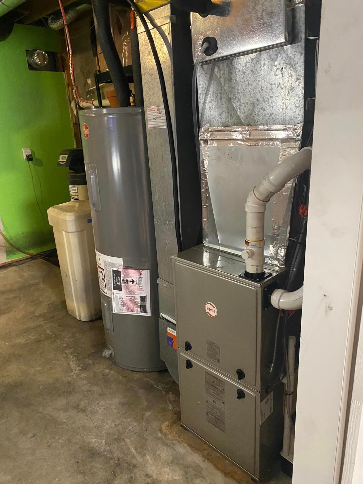A basement with a water heater, water filter, furnace, and ductwork against a green painted wall.