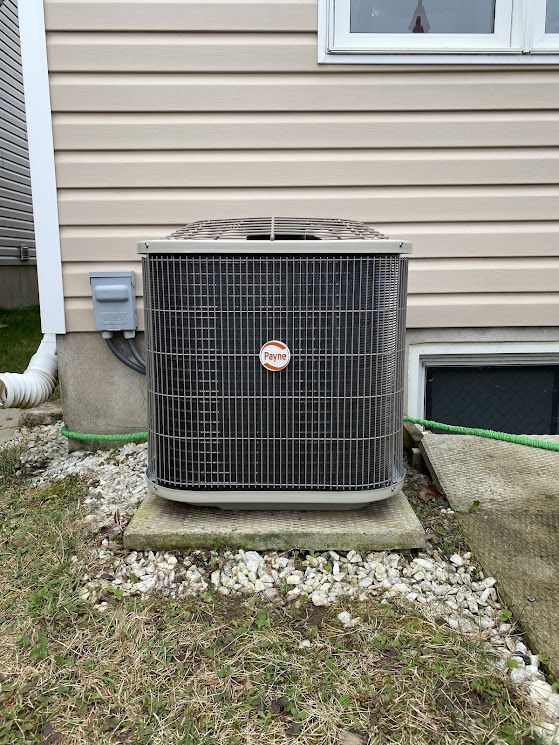 A Rheem air conditioner unit outside a house, on a concrete base, next to the foundation.