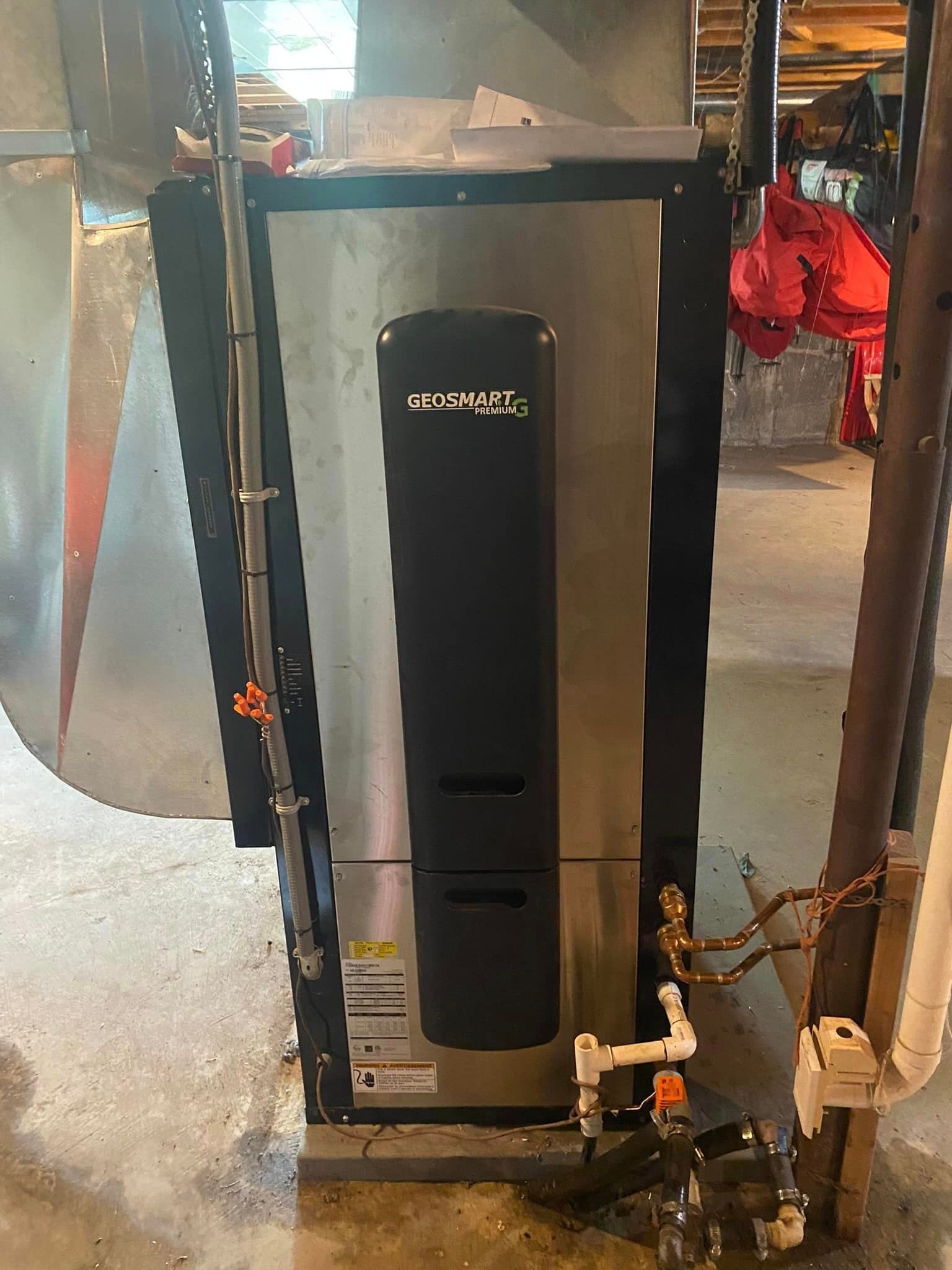 Silver and black furnace in a basement with attached ductwork and pipes.