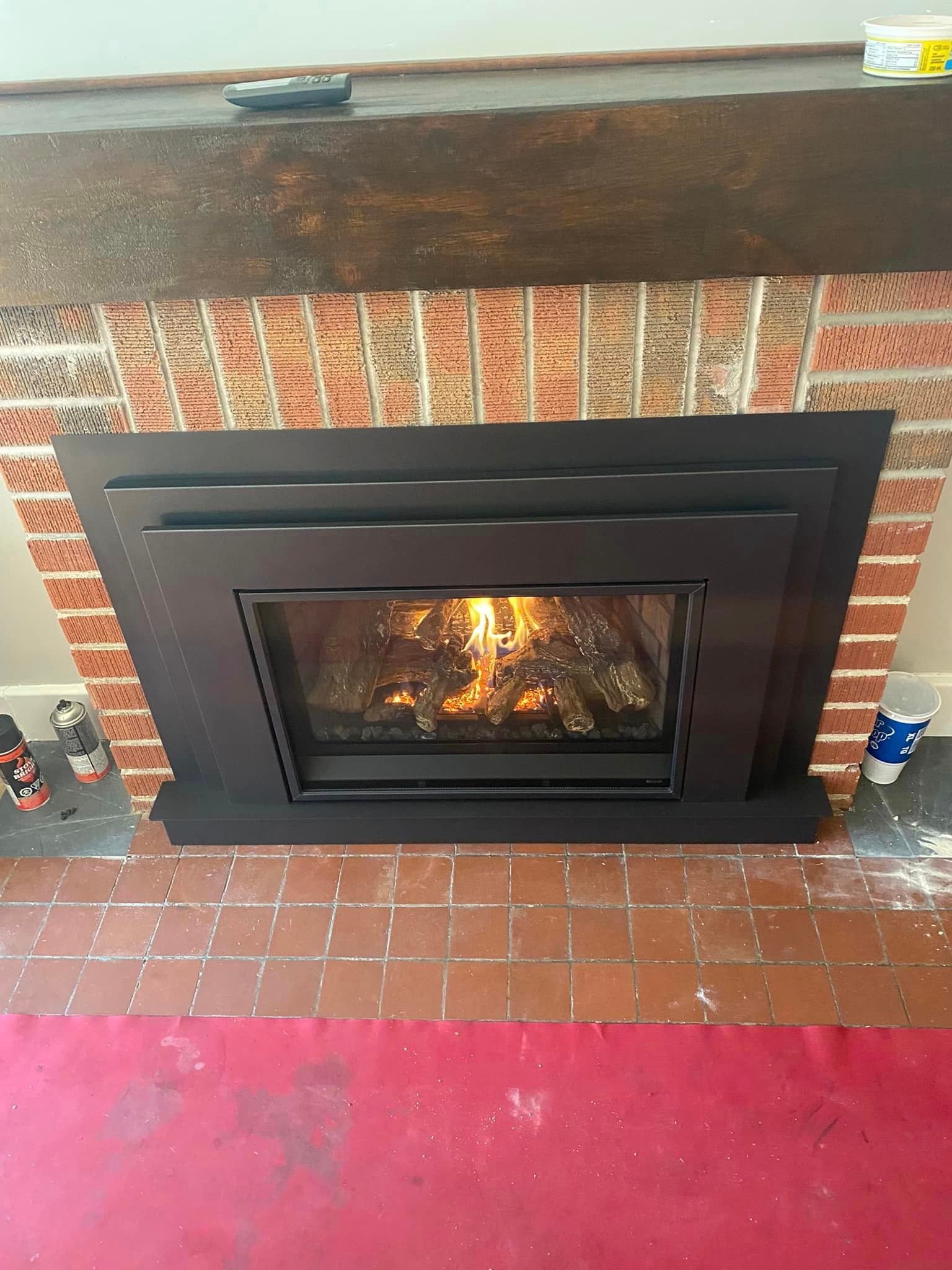 Black fireplace with glowing flames against a brick wall and a red rug.