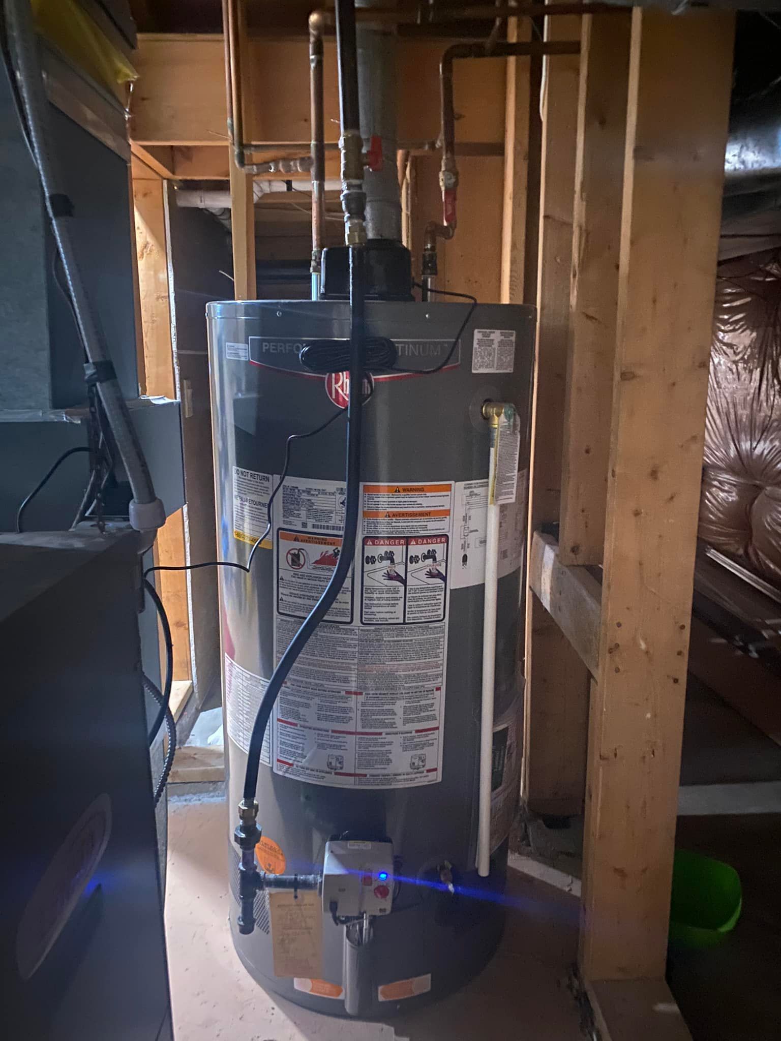 Water heater in a basement framed with wood. Pipes and a gas line are connected.