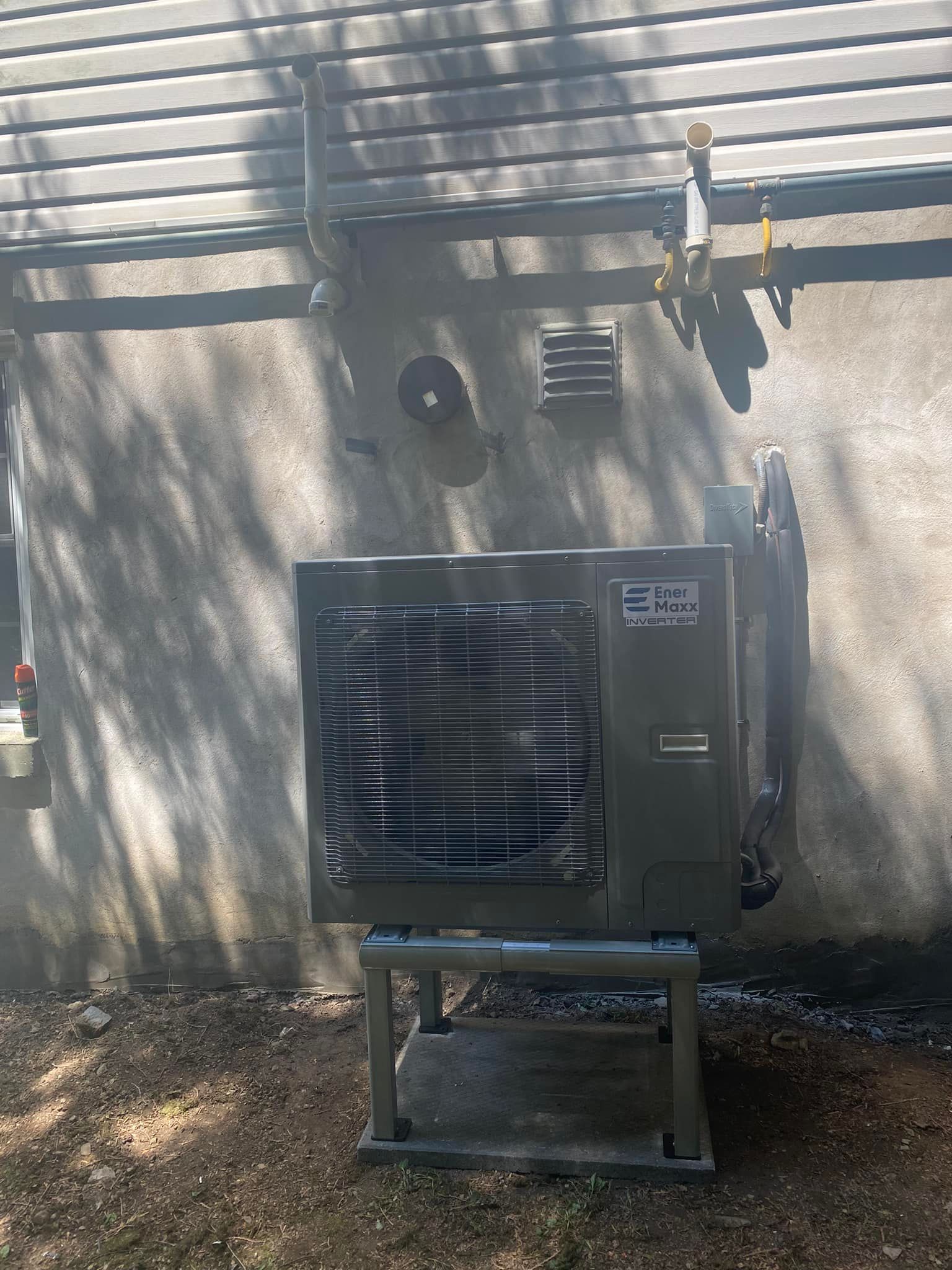Air conditioning unit mounted on a metal stand outside a building with a stucco wall.
