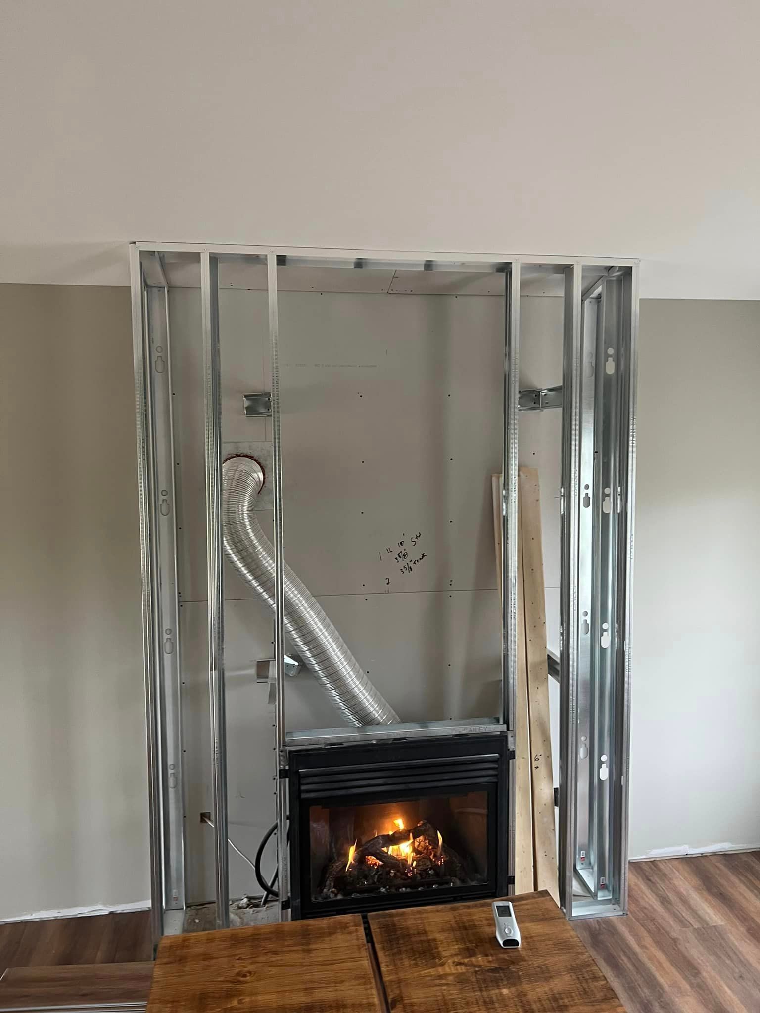Fireplace under construction; metal framing surrounds a gas fireplace with flames.