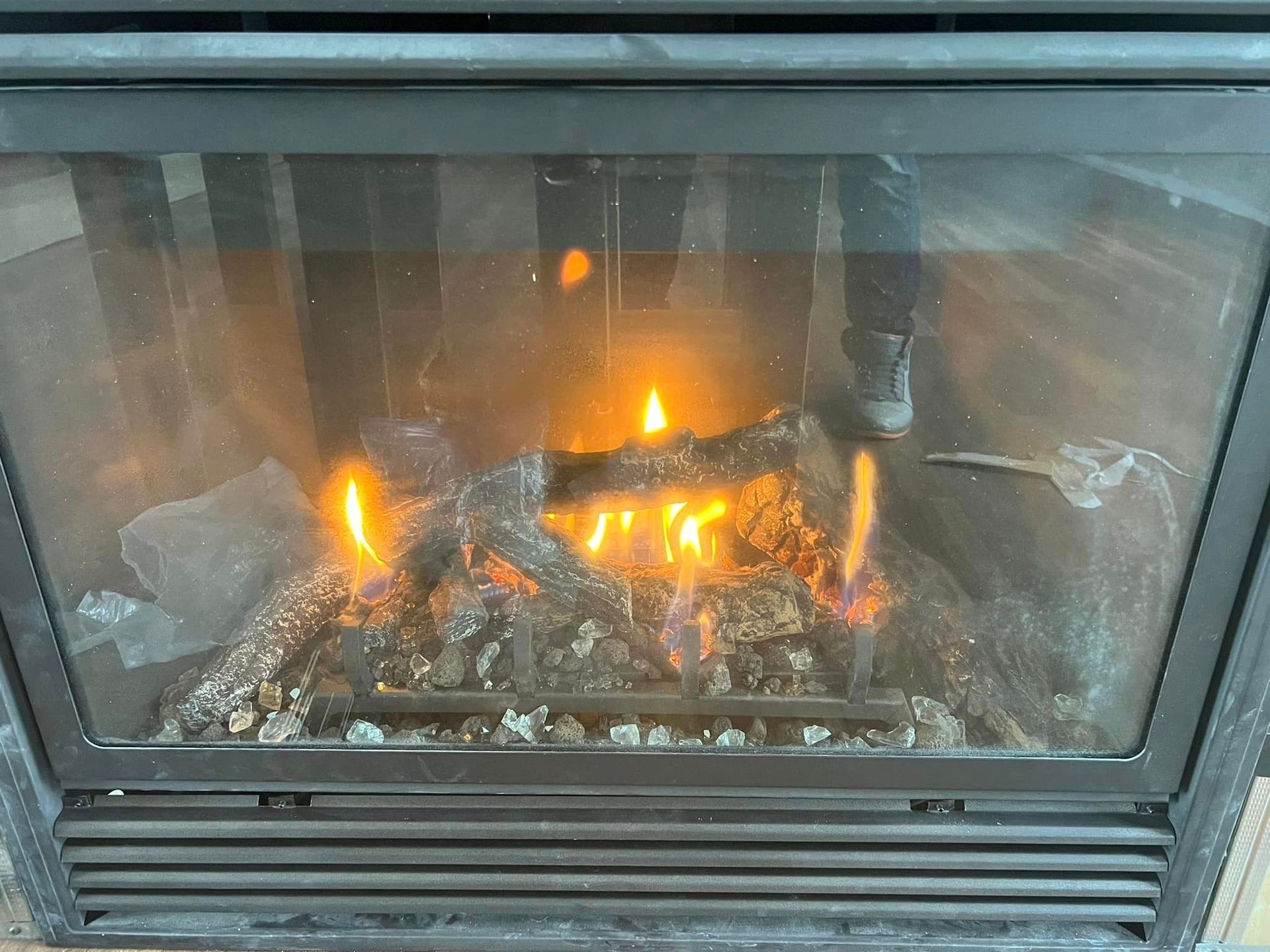 A gas fireplace with burning logs, emitting orange flames. The glass door is visible, with a dark frame.