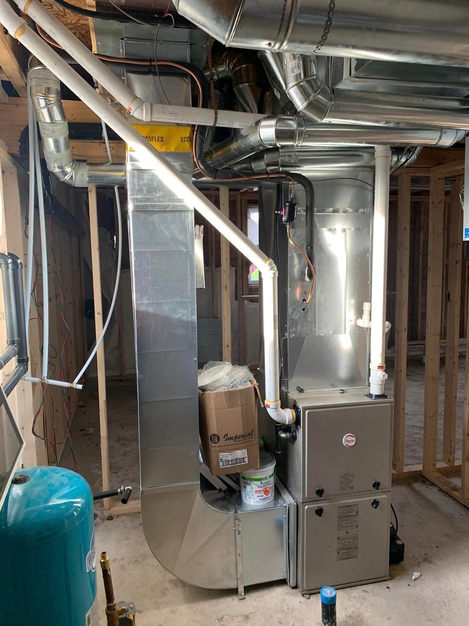 Furnace installation in a wooden-framed basement, with ductwork, pipes, and a water tank.