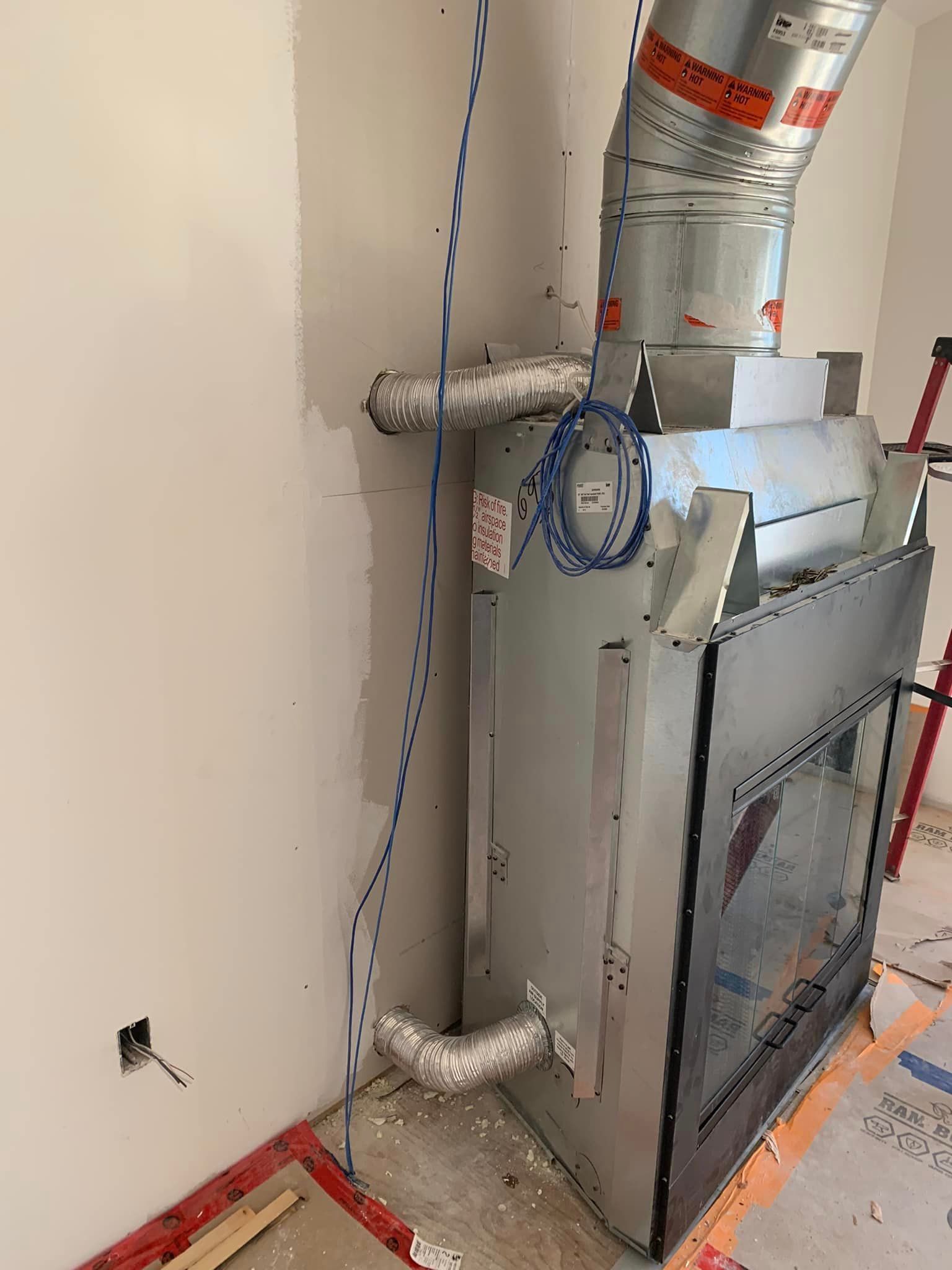 HVAC unit installed, ductwork connected. Metallic silver, against white wall. Electrical wires present.