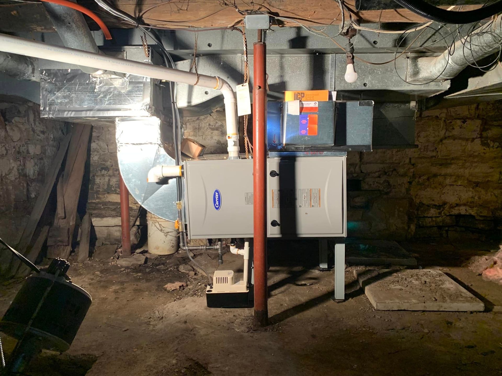 Furnace in a basement; silver and gray, with ductwork and a filter. Brick walls and dim lighting.