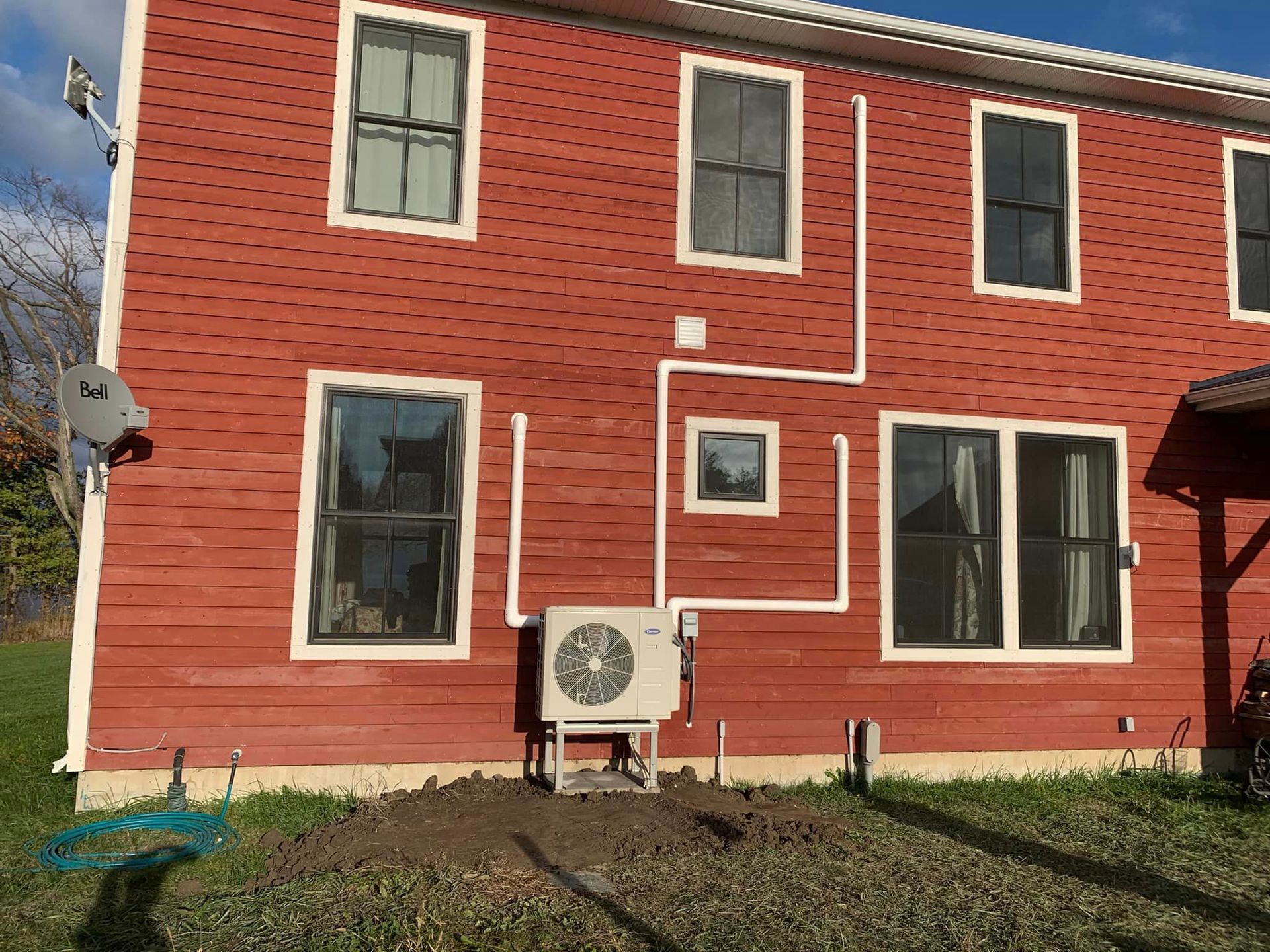 Red building with windows, a heat pump, and white piping on the side.