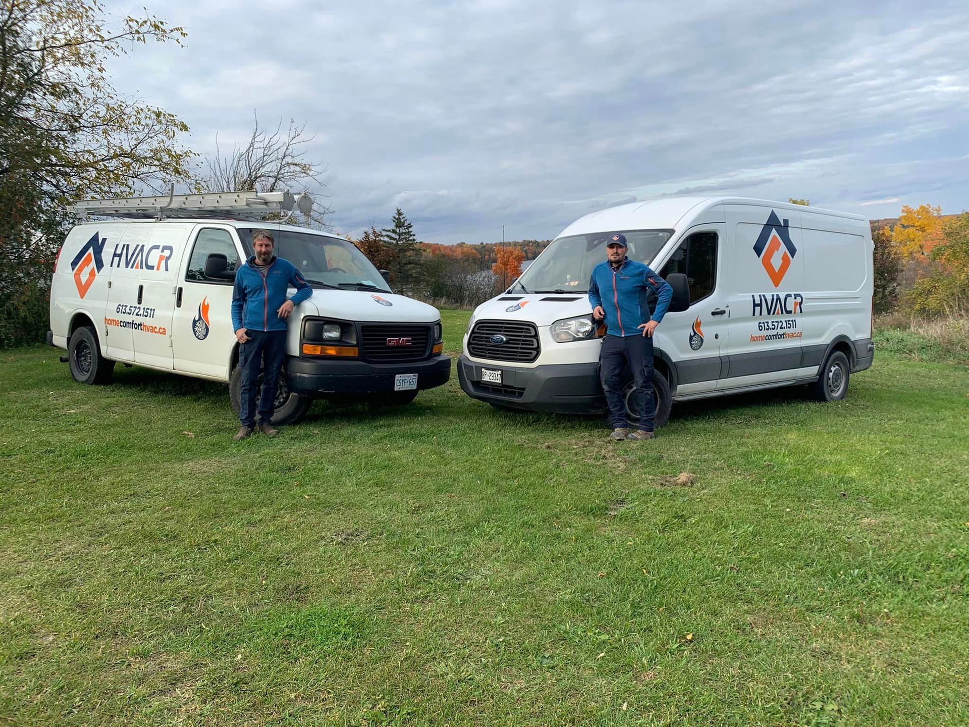 Two men stand near their HVAC service vans on a grassy field.