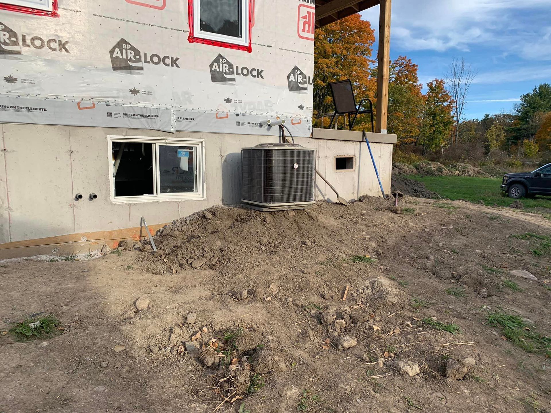 HVAC unit installed at the base of a newly constructed house, on a dirt hill.