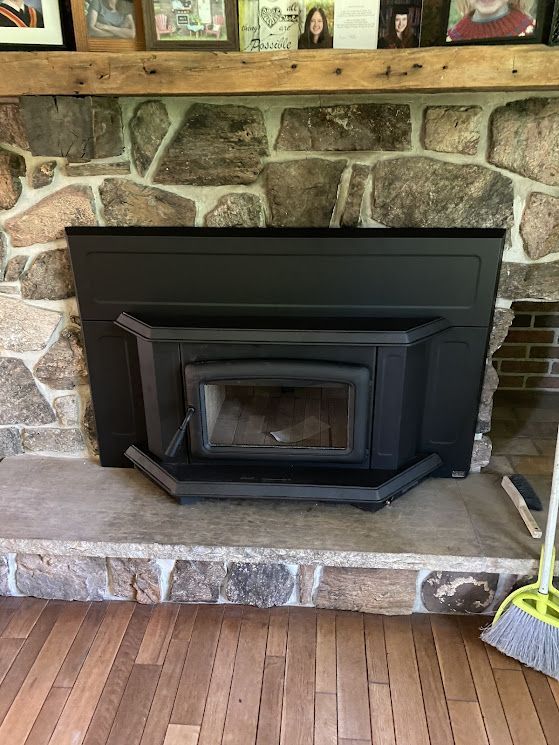 Black fireplace with a stone background, set on a stone hearth, with wooden floor.