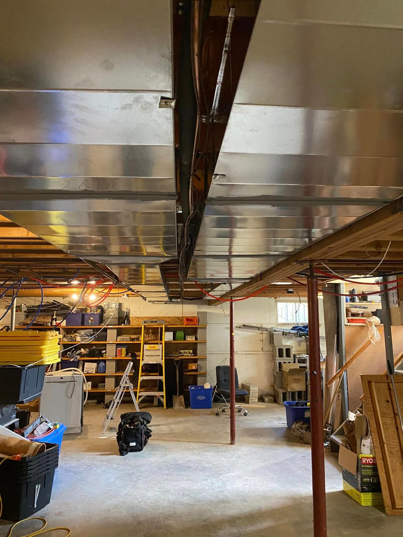Basement ceiling with metal ductwork and exposed wooden beams. Storage shelves and clutter line the walls.