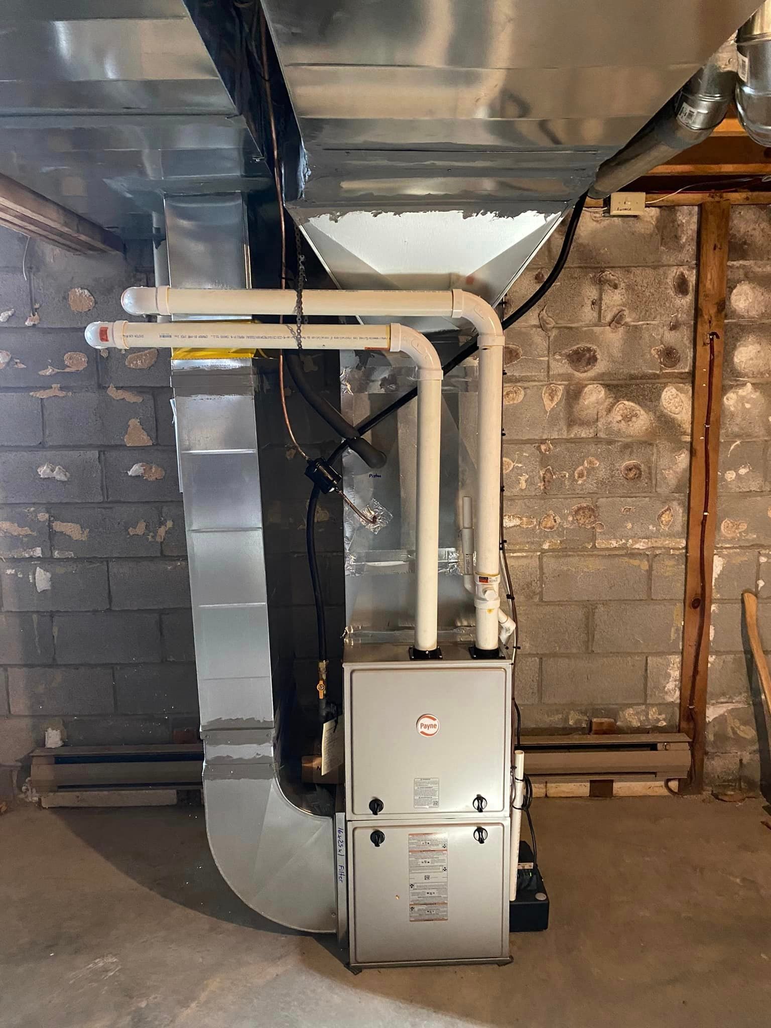 Furnace in basement with ductwork, pipes, and cinderblock wall.