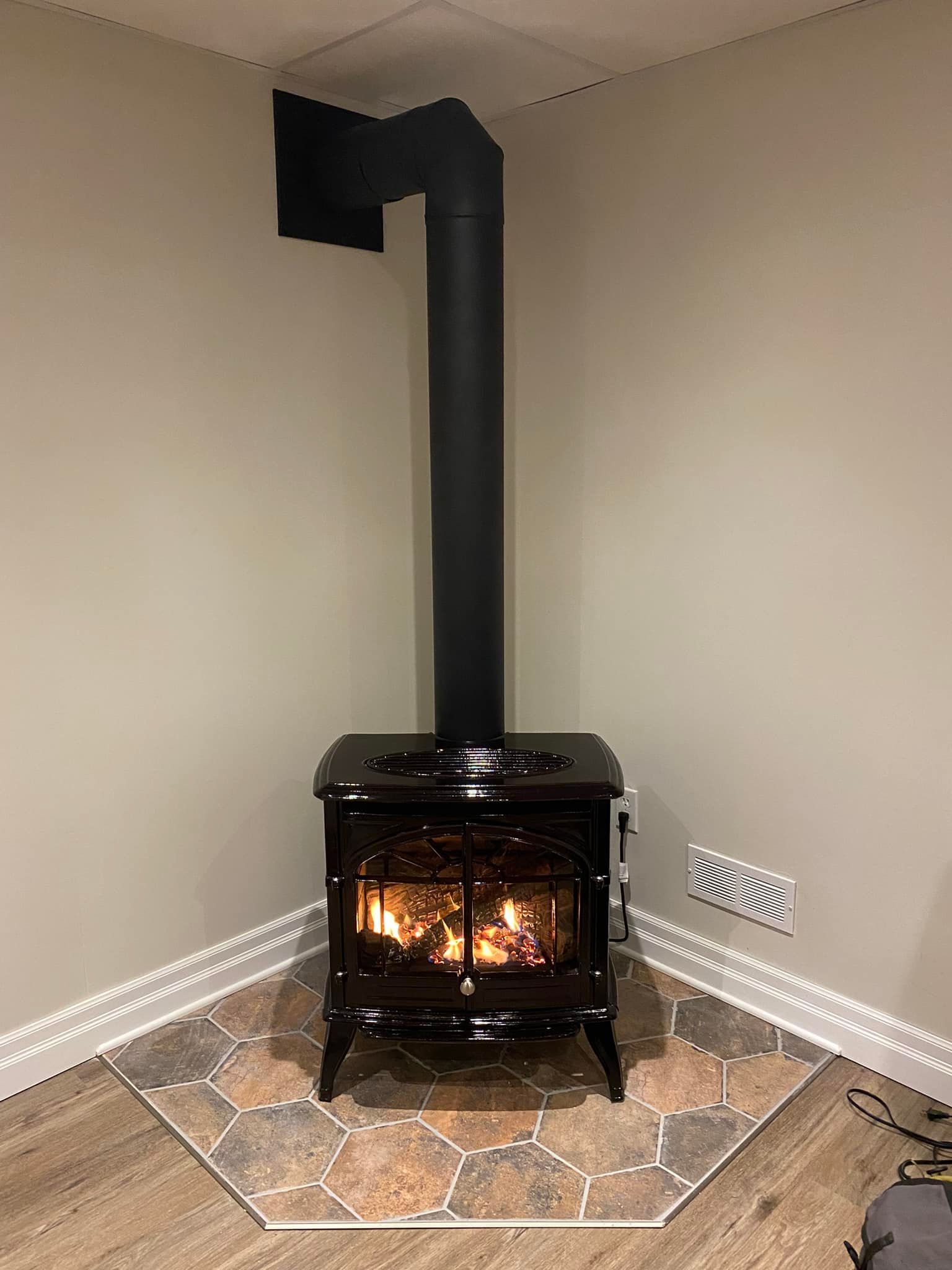 A black wood-burning stove in a corner of a room with a black chimney pipe against tan walls.