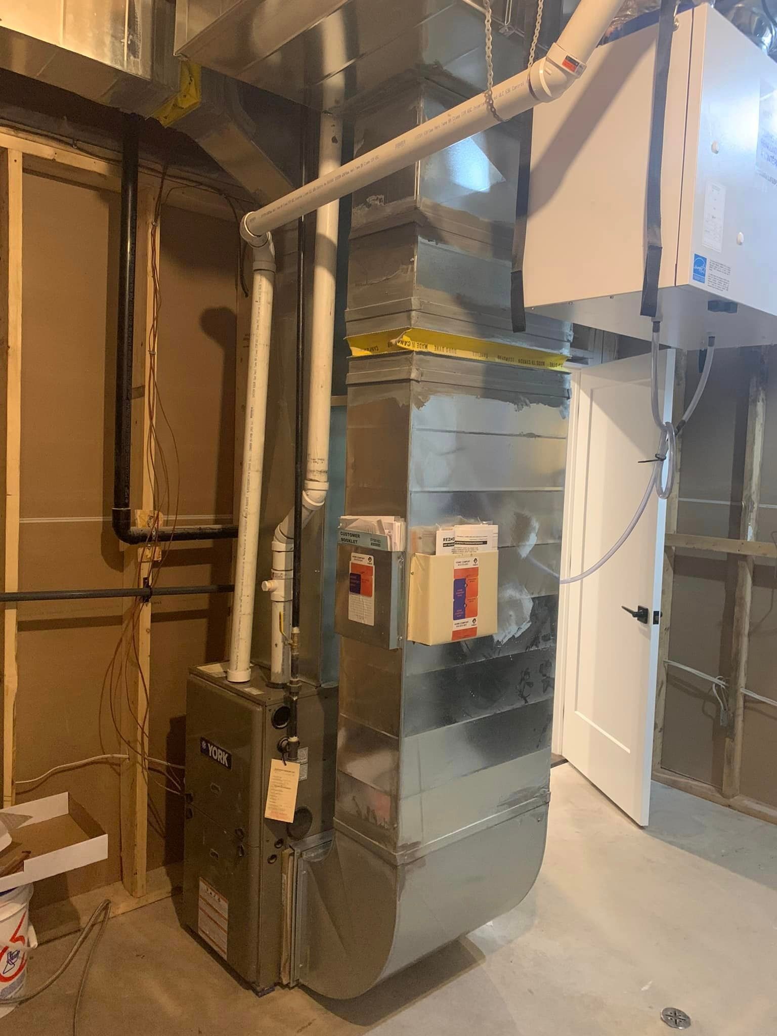 Furnace and ductwork in a basement next to a white door.