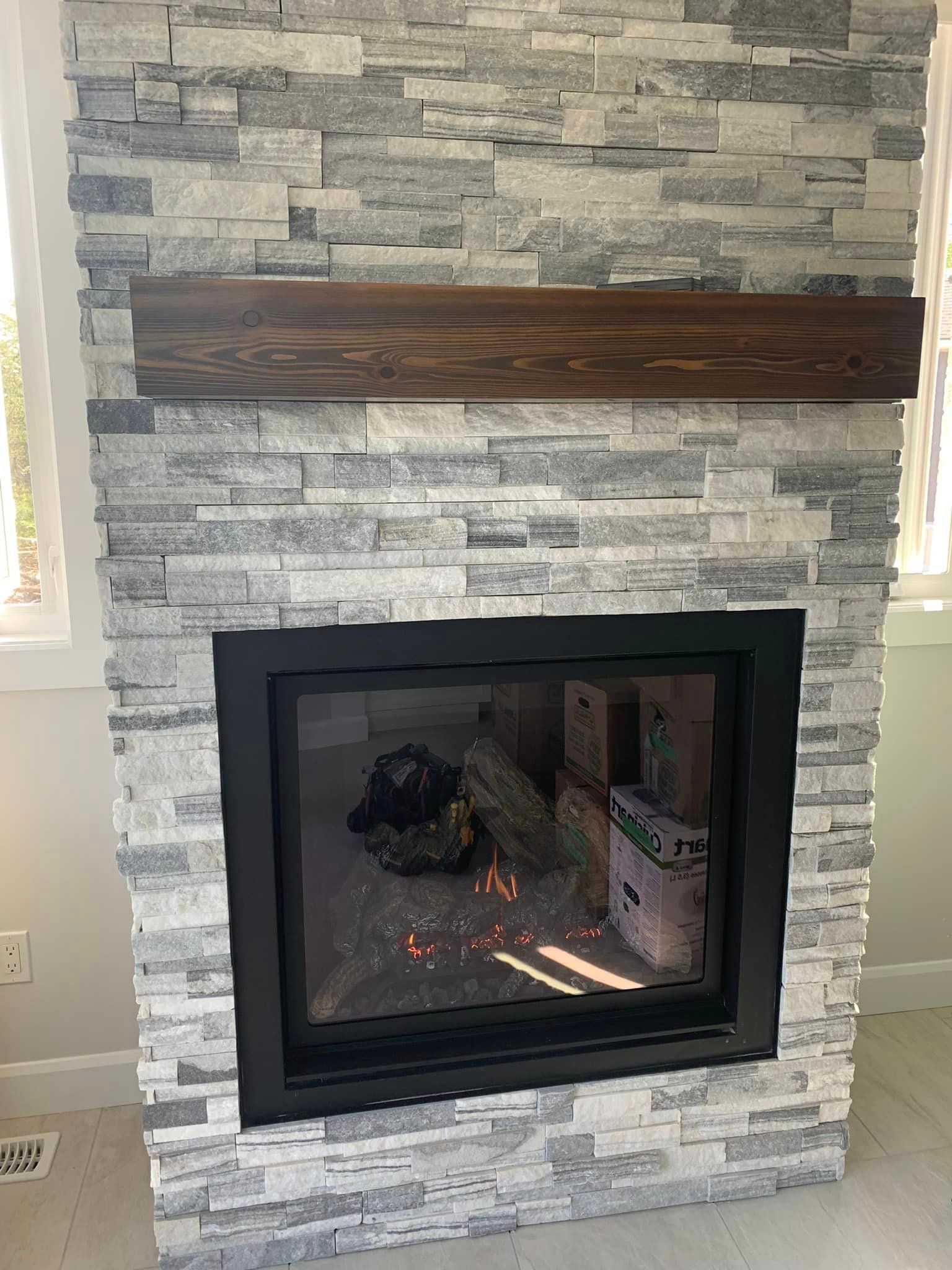 Fireplace with gray stone facade, black frame, and wooden mantel.