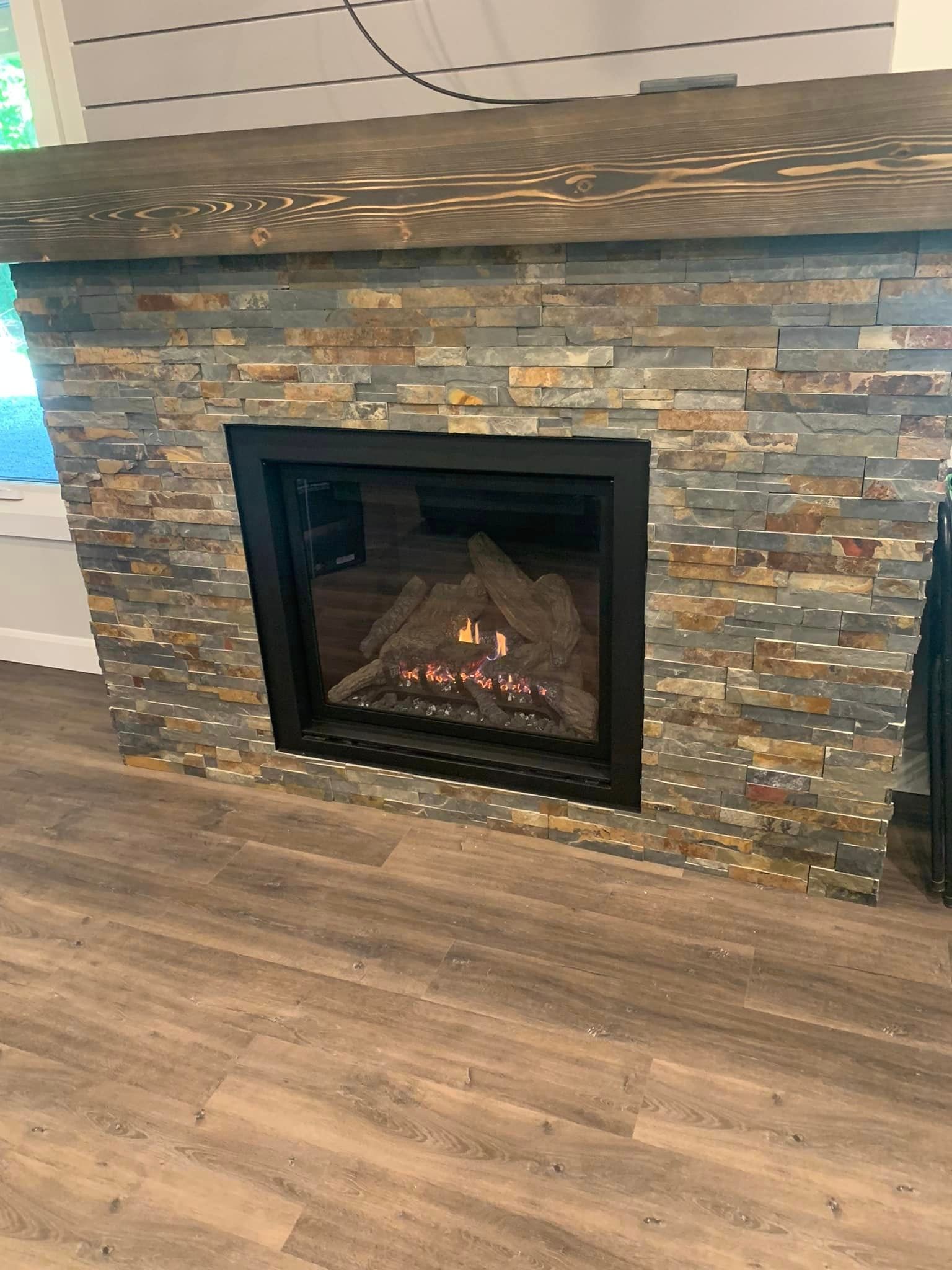 Fireplace with stone veneer, dark frame, and a lit fire.