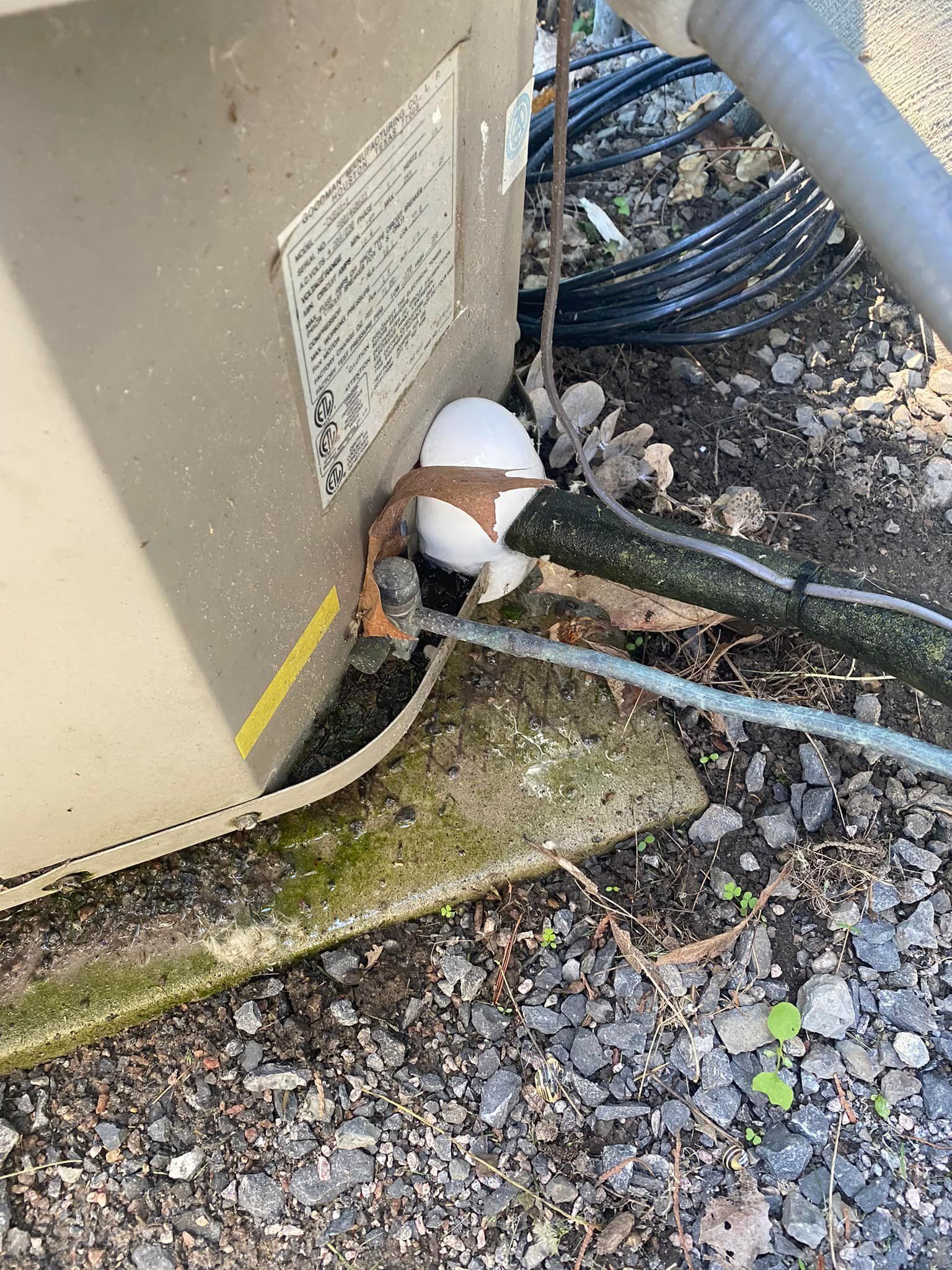 An air conditioning unit with cracked insulation near base, in an outdoor setting.