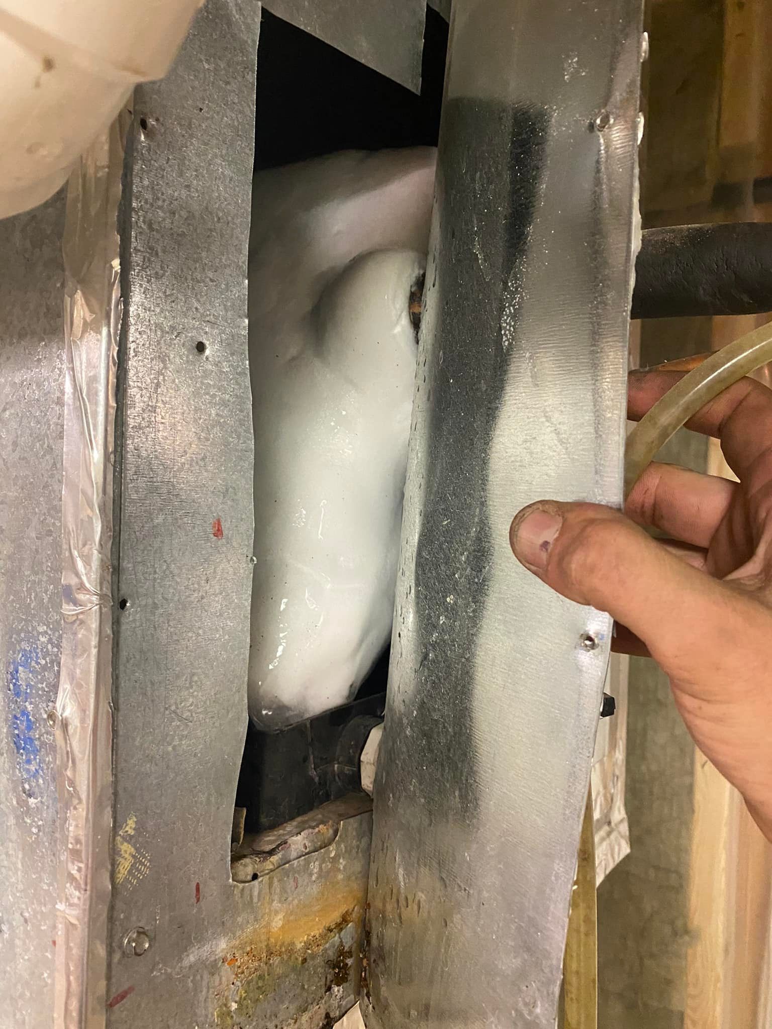 Ice buildup inside a metal air conditioning unit. A hand holds a tube.