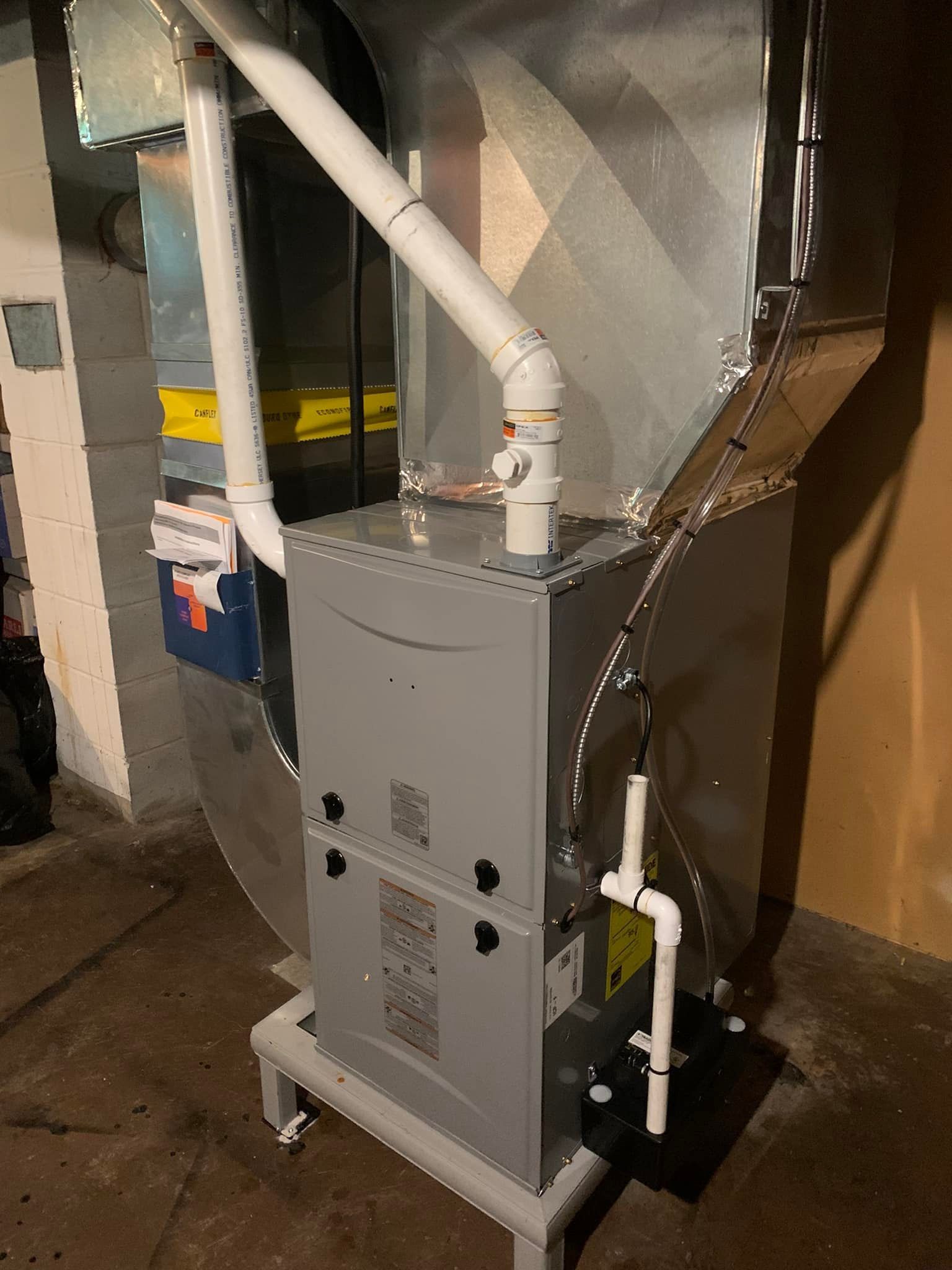 A gas furnace in a utility room with white pipes and silver ducts.