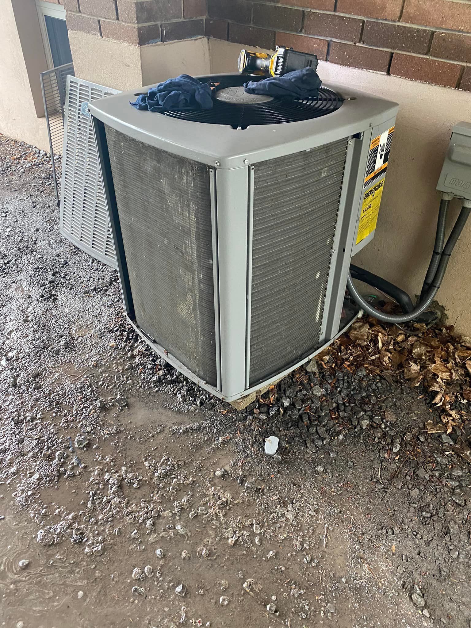 AC unit outside on a concrete surface, surrounded by gravel and debris.