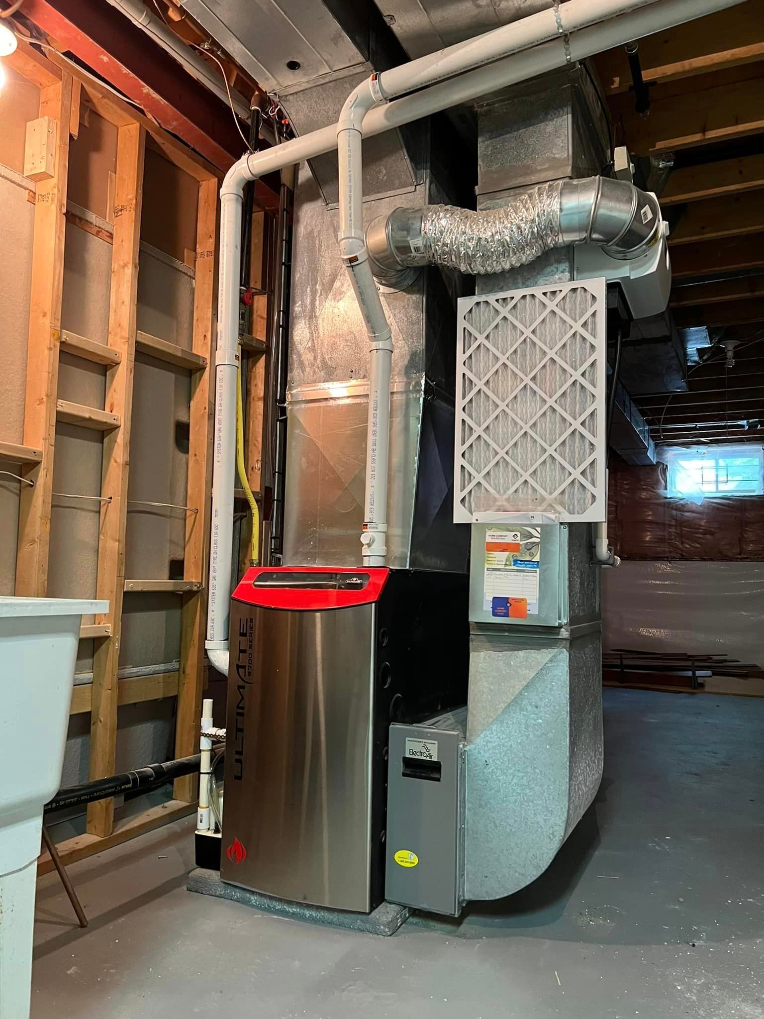 Furnace in a basement. Stainless steel unit with ductwork, filter, and pipes.
