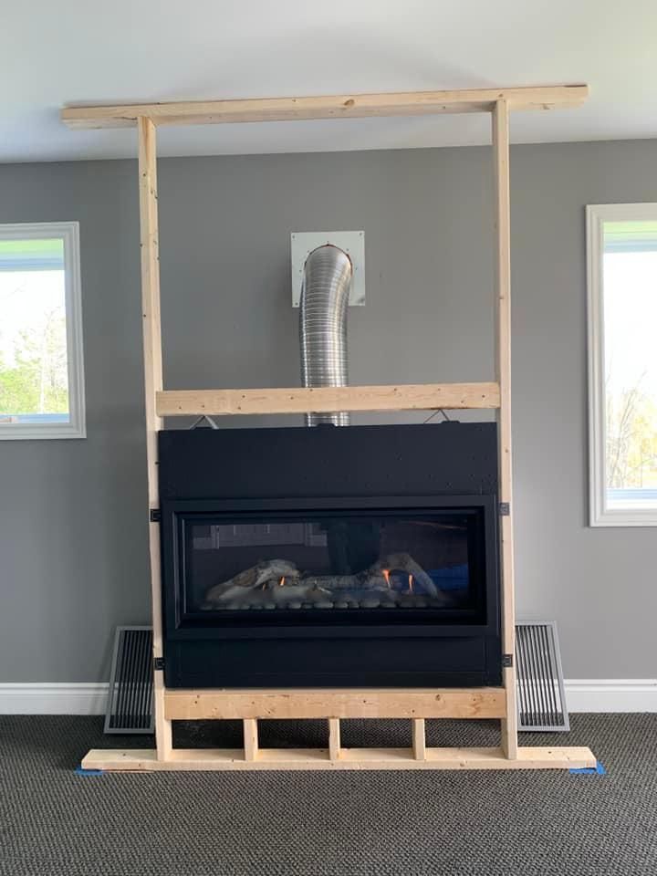 Fireplace installation: black unit framed by wood, with venting and partially framed drywall.