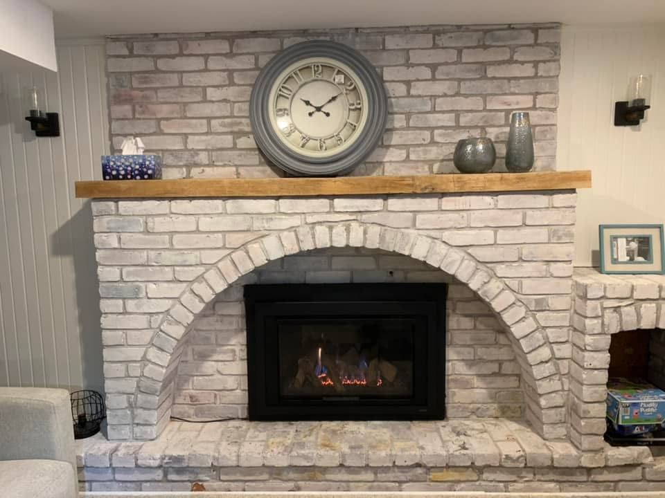 Brick fireplace with an arched opening, clock, and decorative items.