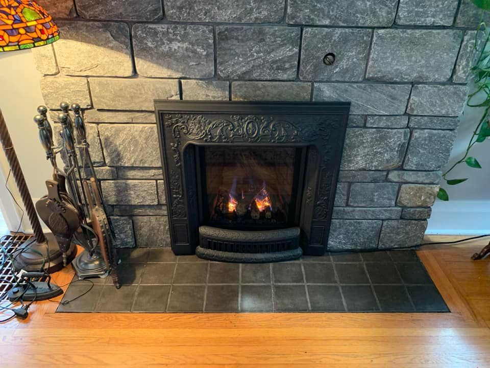 Fireplace with lit flames and black cast iron front set in stone, with tools.