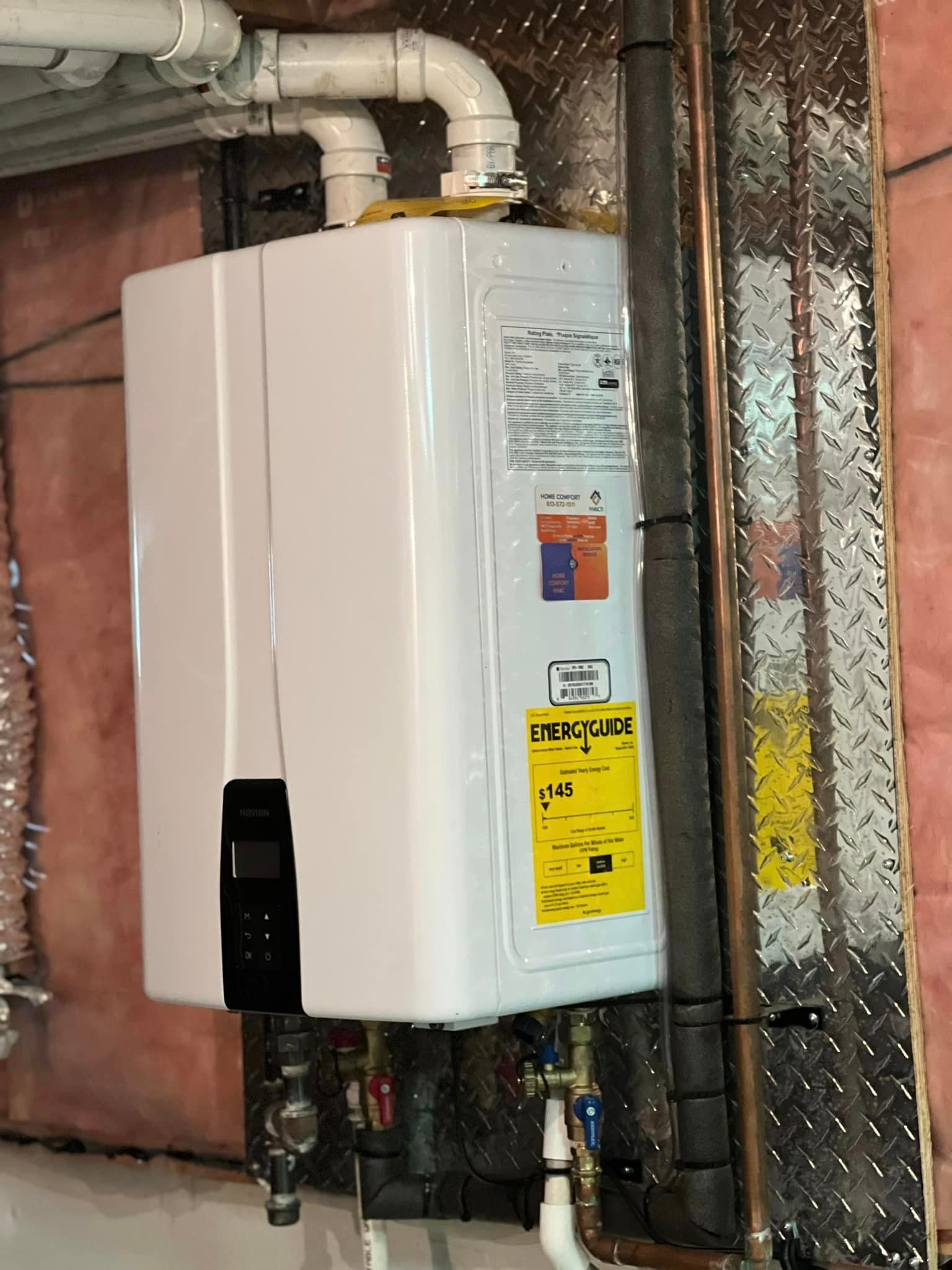 White tankless water heater mounted on a basement wall with pipes.