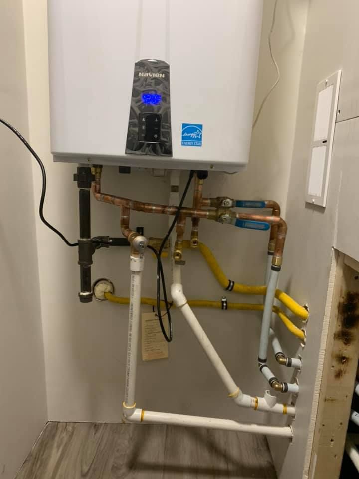 A wall-mounted, white tankless water heater with copper and PVC pipes, and yellow gas lines.