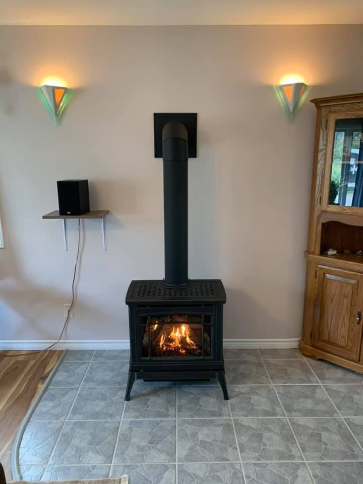 Black wood-burning stove with lit flames, centered against a pale pink wall with two sconces, and a wooden cabinet.