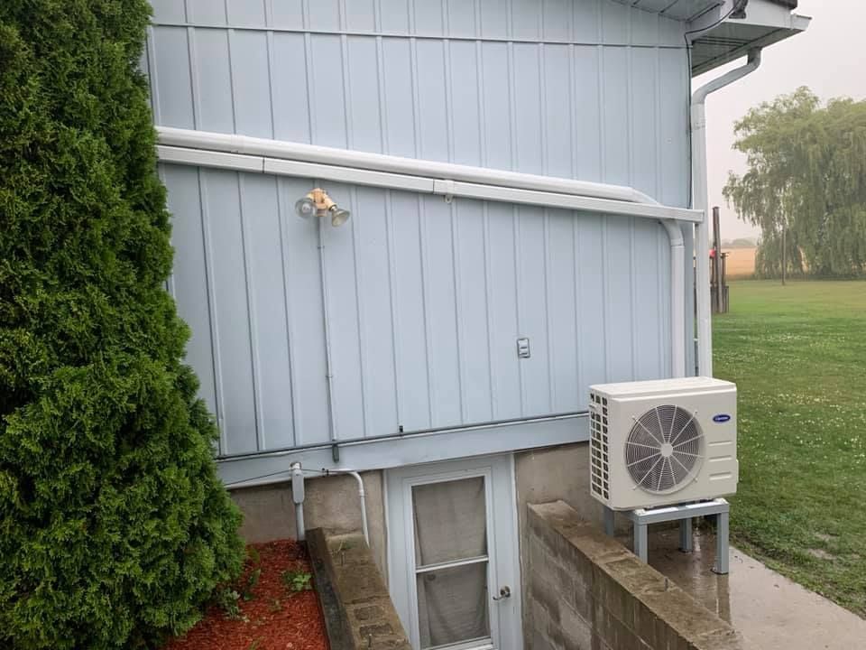 Exterior of a blue house with an AC unit. Green grass, concrete stairs, and a tall green bush are present.