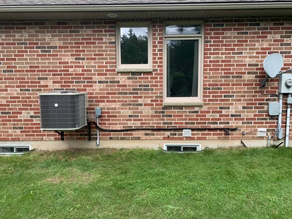 Brick building exterior with AC unit, two windows, and electrical components. Green grass in the foreground.