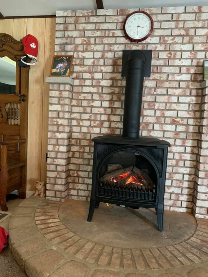 Black electric fireplace with flames, against a brick wall with a clock, in a room.