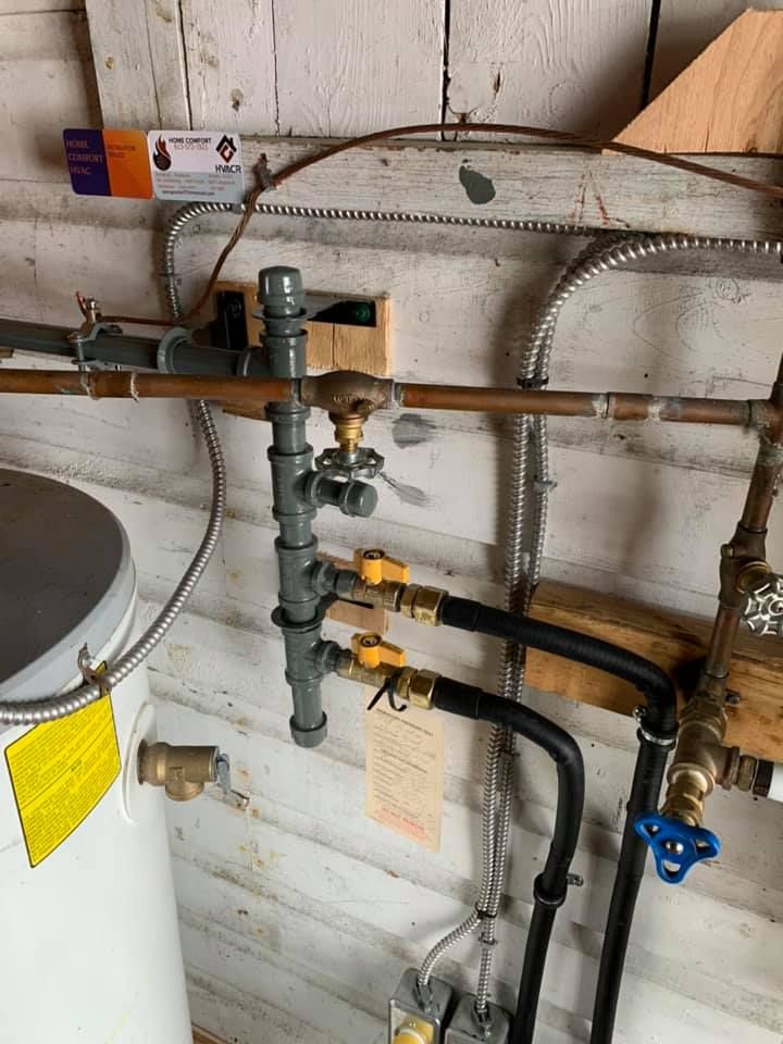 Gas pipes and valves attached to a water heater and wall in a utility room.