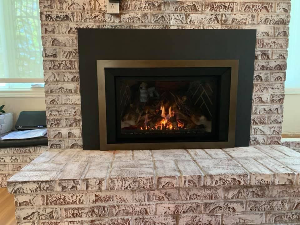 Fireplace with brick surround and a black and gold frame, fire burning.