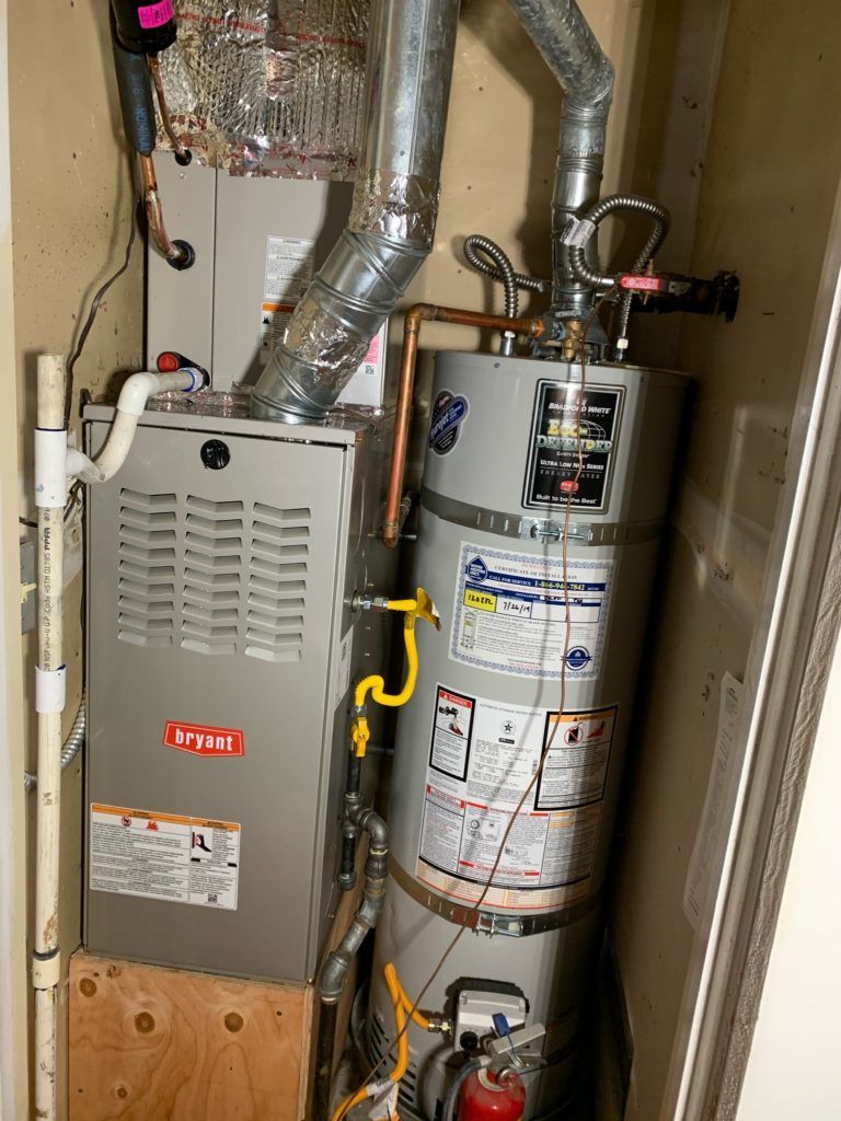 Furnace and water heater in a utility closet. Gray and silver appliances with various pipes.