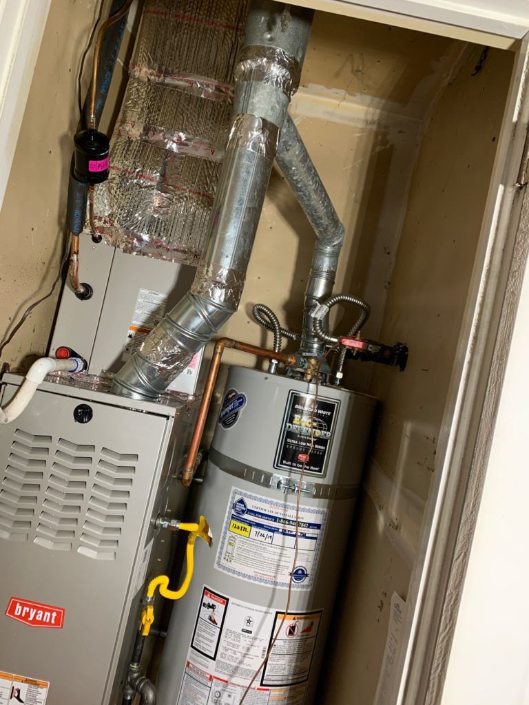 Furnace and water heater in a utility closet with vent pipes, electrical wiring, and a yellow gas line.