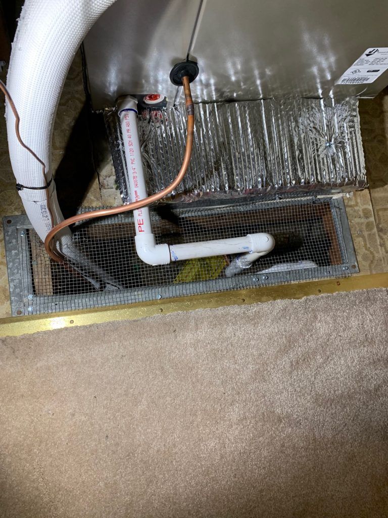 HVAC drain pipe assembly with white PVC pipe, copper tubing, and ductwork on carpeted floor.