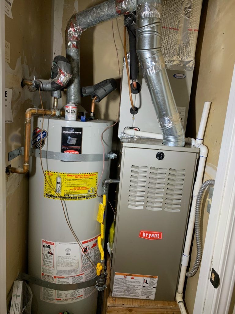 Water heater and furnace in a utility closet with vent pipes and wiring.