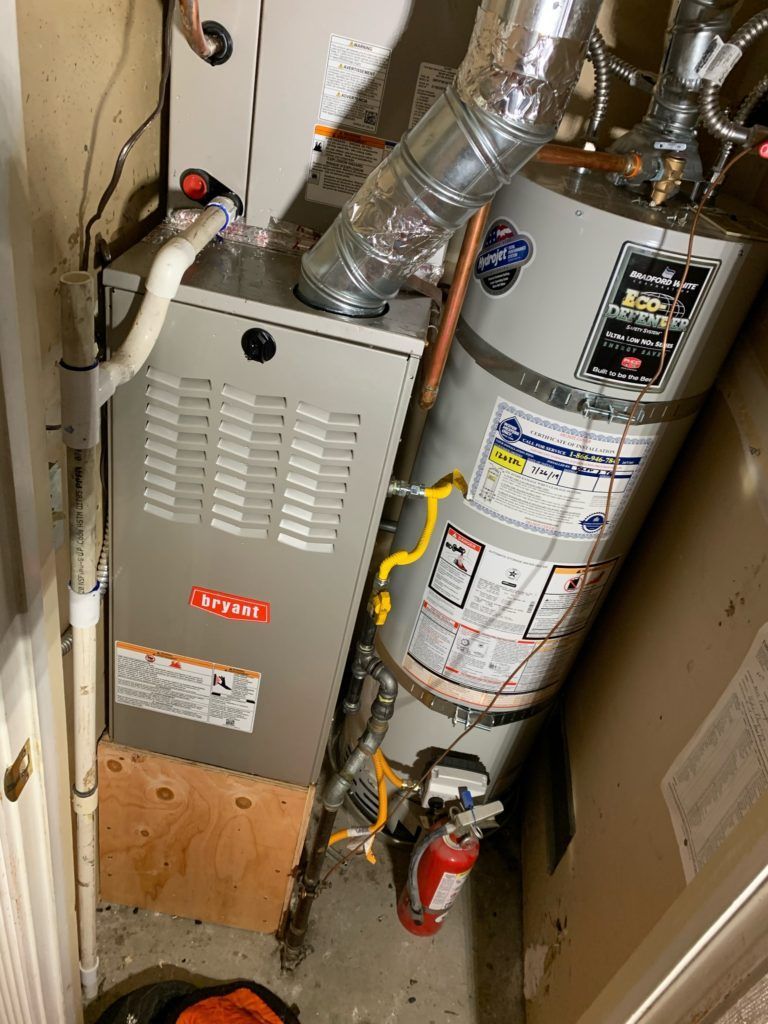 Furnace and water heater in a utility closet. Gray Bryant furnace, silver water heater, white ducting, red fire extinguisher.