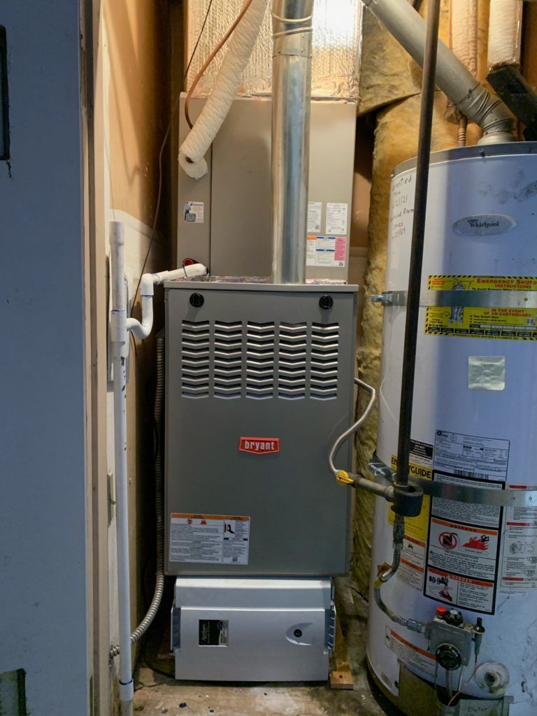 Furnace and water heater in a utility room. Gray Bryant furnace, white water heater, and connecting pipes.